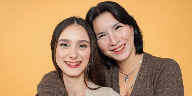 Une mère passe son bras autour des épaules de sa fille adolescente, toutes deux sourient.