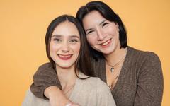 Une mère passe son bras autour des épaules de sa fille adolescente, toutes deux sourient.